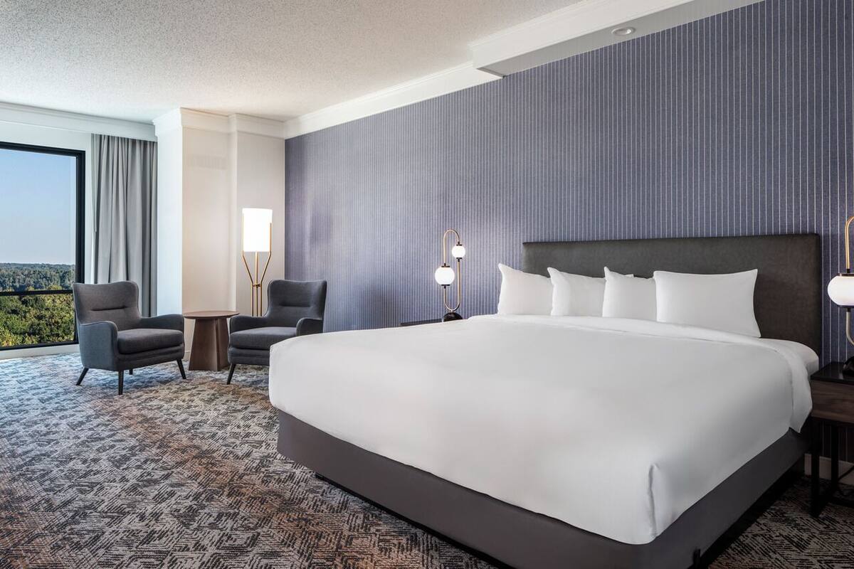 A hotel room with a large bed, two armchairs, a small table, and a lamp.
