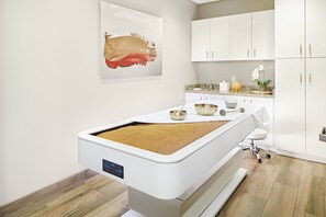 A modern medical treatment room with a treatment table, cabinets, and a painting on the wall. - Horseshoe Tunica - A Caesars Rewards Destination (Robinsonville)