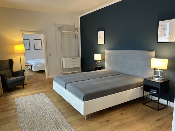 Un dormitorio moderno con cama, mesitas de noche, una silla, armario y una lámpara de pie.