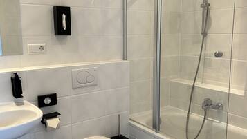 A modern bathroom with a glass-enclosed shower, a white sink, and a toilet.