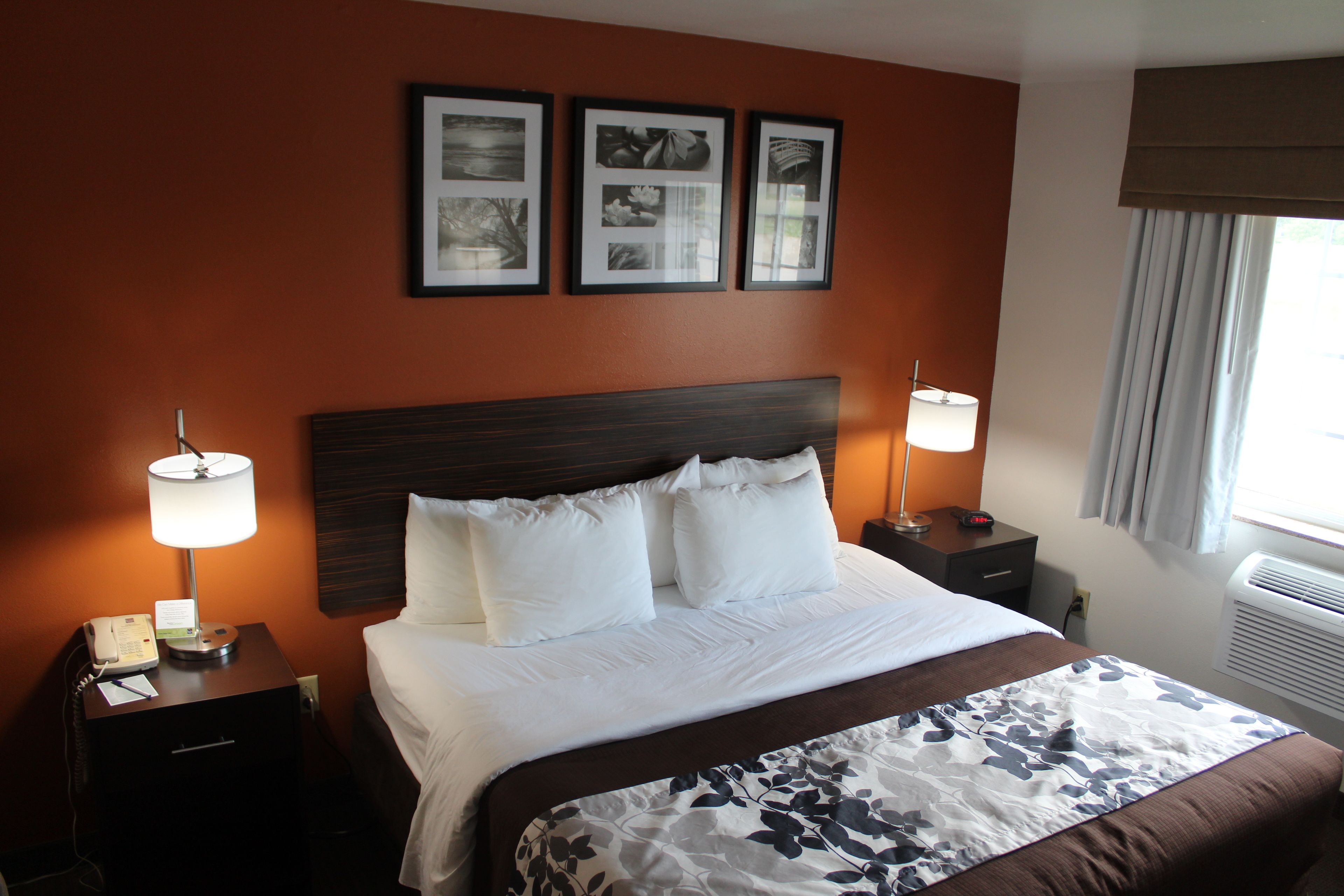 A hotel room with a large bed, two bedside tables with lamps, a wall-mounted telephone, and framed pictures above the bed.