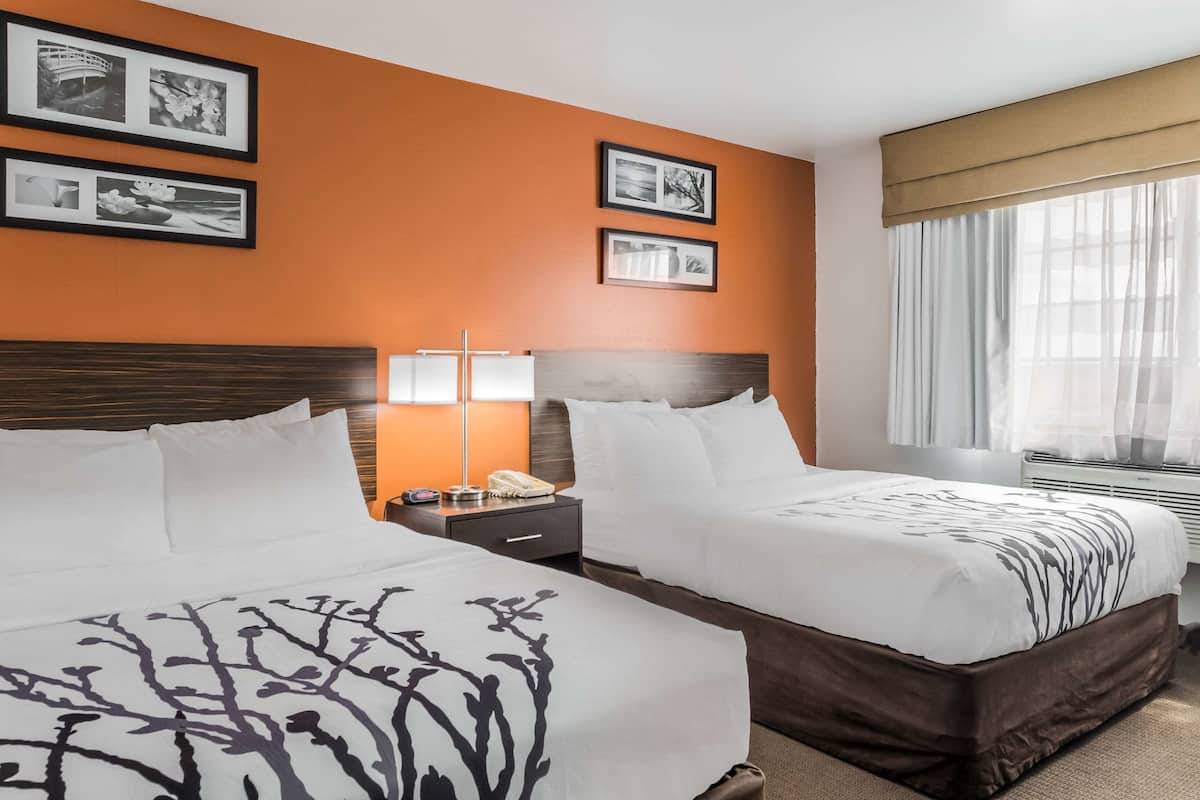 Een hotelkamer met twee bedden, een nachtkastje met een lamp, een telefoon en ingelijste foto’s aan de muur.