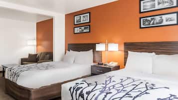 A hotel room with two beds, a nightstand, a lamp, and framed pictures on the wall.