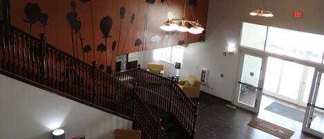 A hotel lobby with a wooden staircase, a reception desk, and a large window.