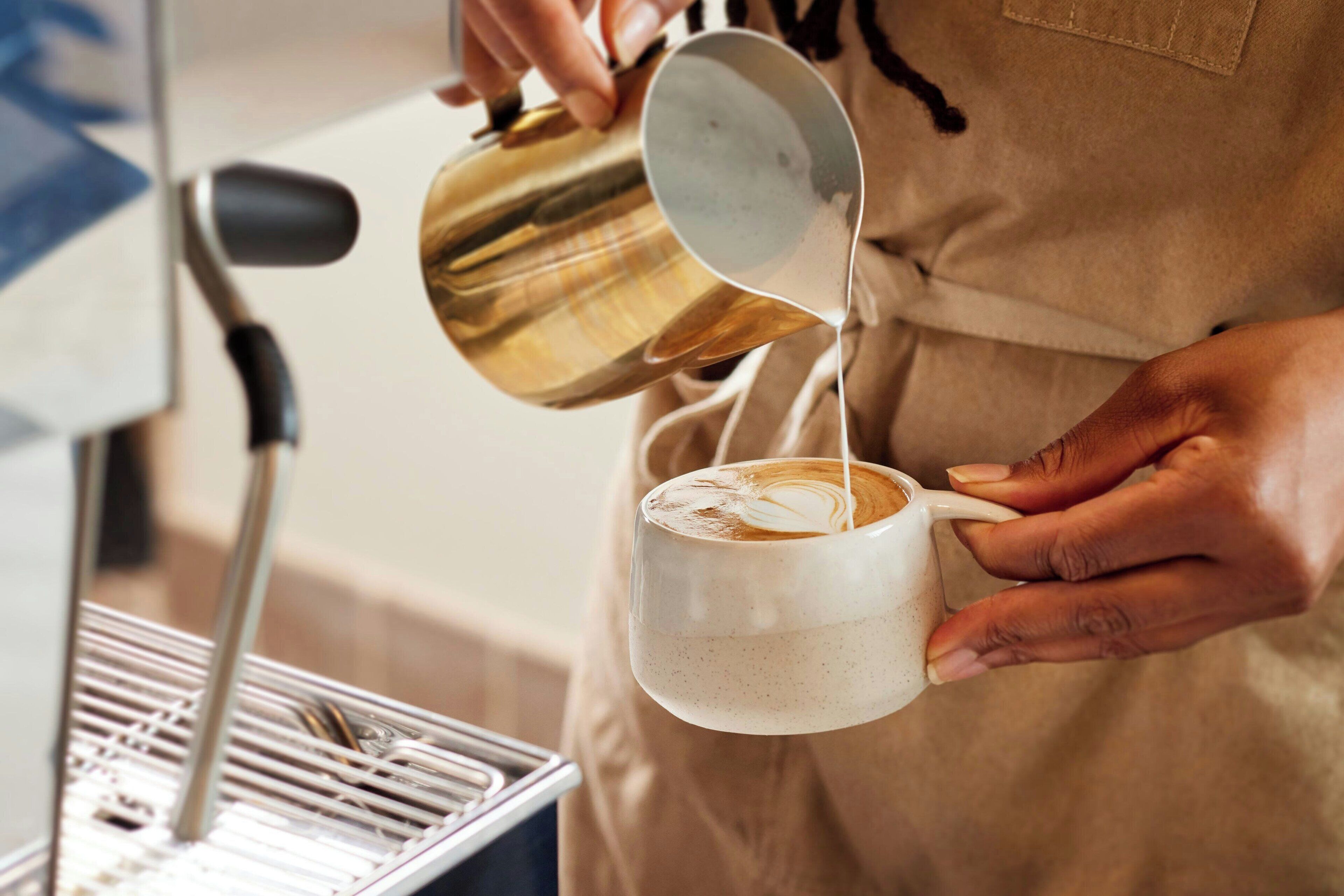 En person häller mjölk i en kopp kaffe.