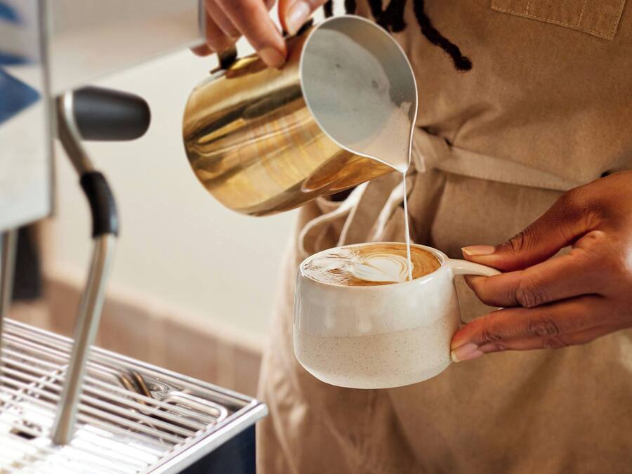 En person häller mjölk i en kopp kaffe.