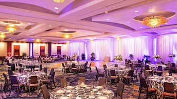 A banquet hall with round tables set for dining, surrounded by chairs, and decorated with floral arrangements.