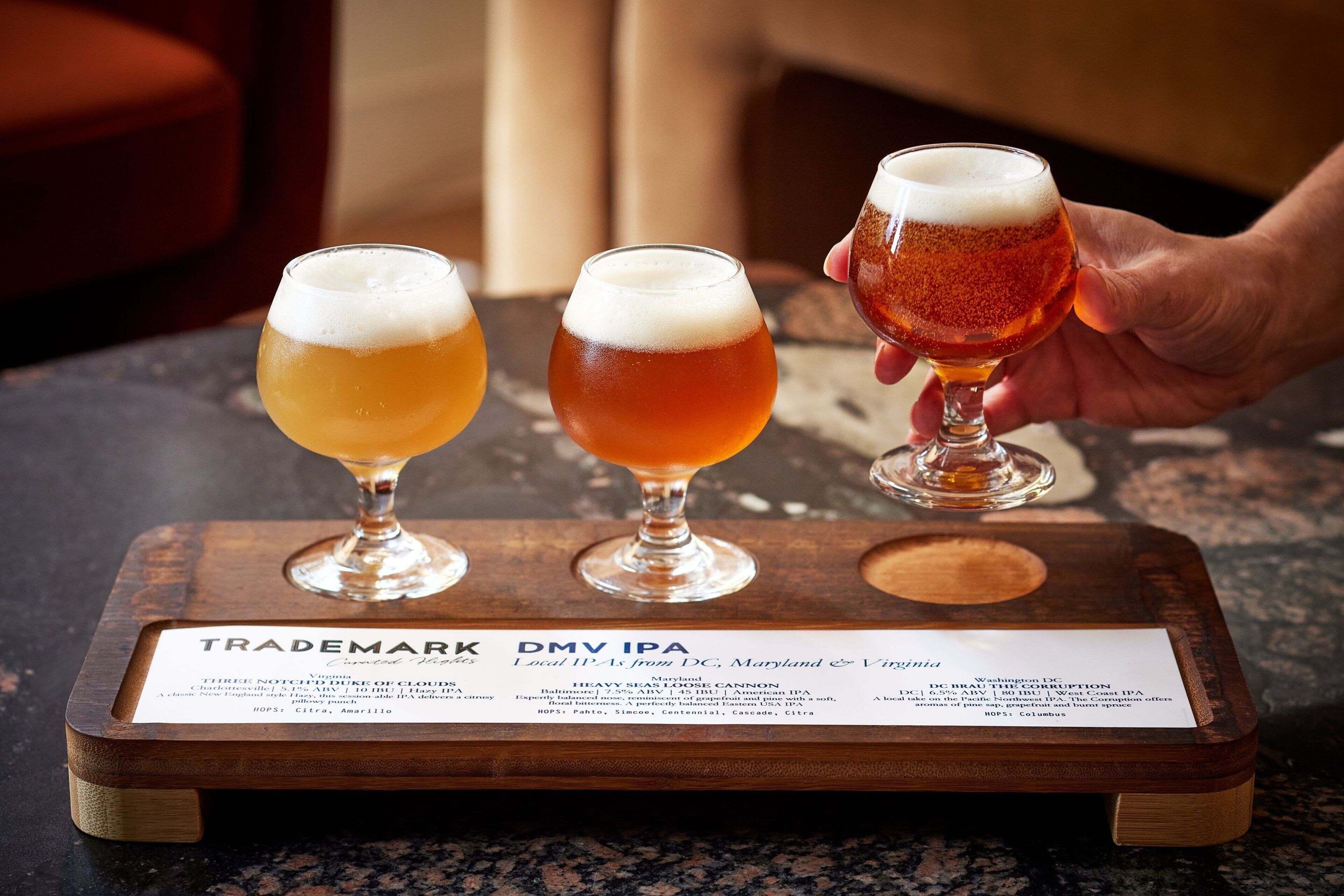 Three glasses of beer on a wooden tray with a label.