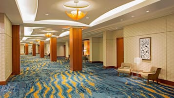 Un amplio vestíbulo de hotel con alfombra estampada, columnas de madera e iluminación moderna.