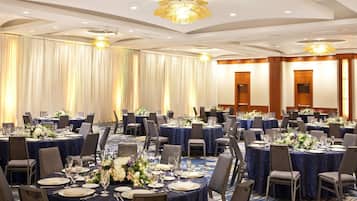 A banquet hall with round tables set for dining, featuring dark blue tablecloths and floral centerpieces.