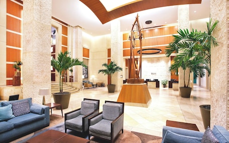 A spacious lobby with a reception desk, seating area, and large potted plants.