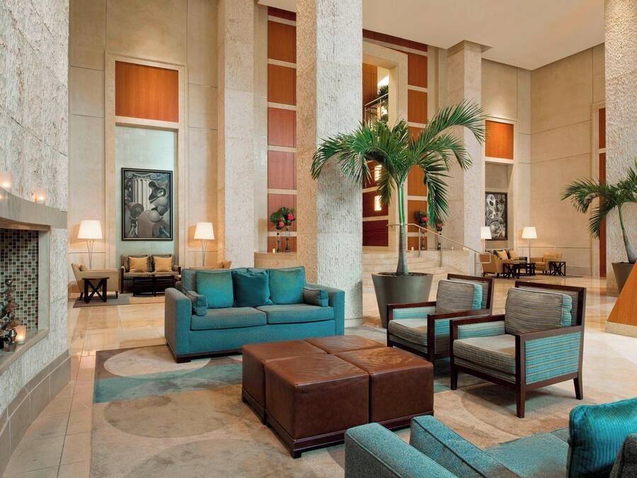 A spacious lobby with a blue sofa, armchairs, a large potted plant, and a fireplace.