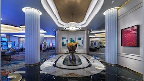 A modern lobby with a marble floor, a central chandelier, and a large vase with flowers.