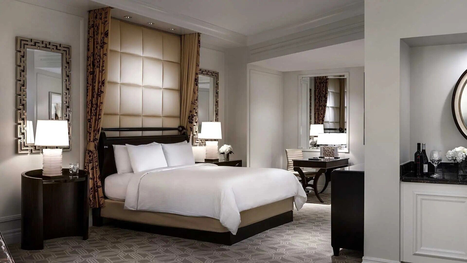 Habitación de hotel con una cama grande, dos mesitas de noche con lámparas, un escritorio con silla y un espejo grande en la pared.