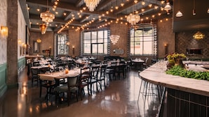 A restaurant with multiple dining tables and chairs, chandeliers, and large windows.