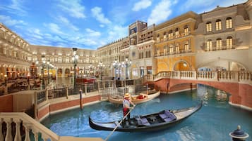 En indendørs kanal i venetiansk stil med gondoler og gondoliere, omgivet af prangende arkitektur og siddepladser.