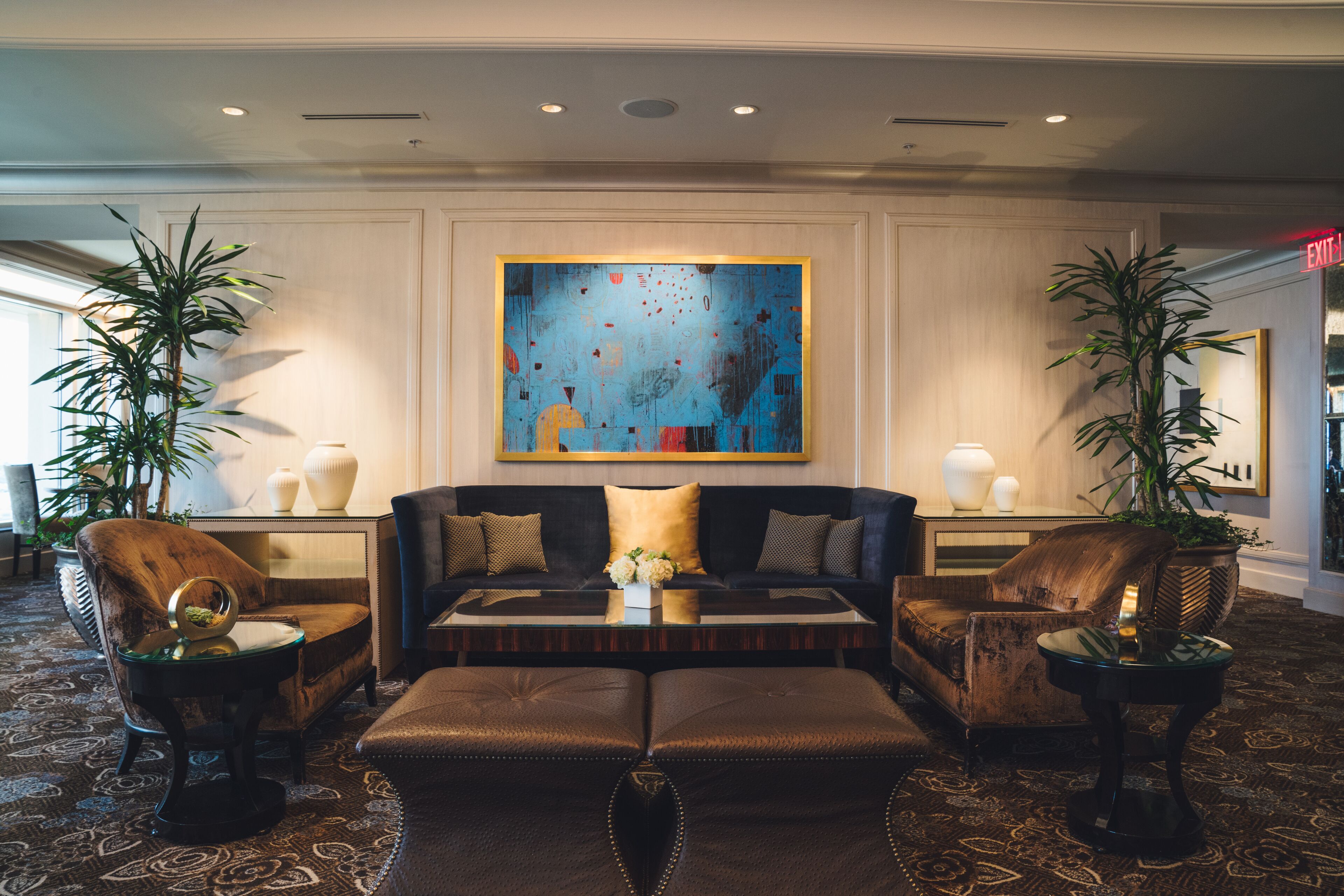Een moderne lobby met een zwarte bank, twee fauteuils, een bijzettafeltje en een groot abstract schilderij aan de muur.