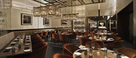Restaurante moderno com pé-direito alto, elegantes lustres e diversos tipos de assentos, incluindo cabines e mesas redondas.