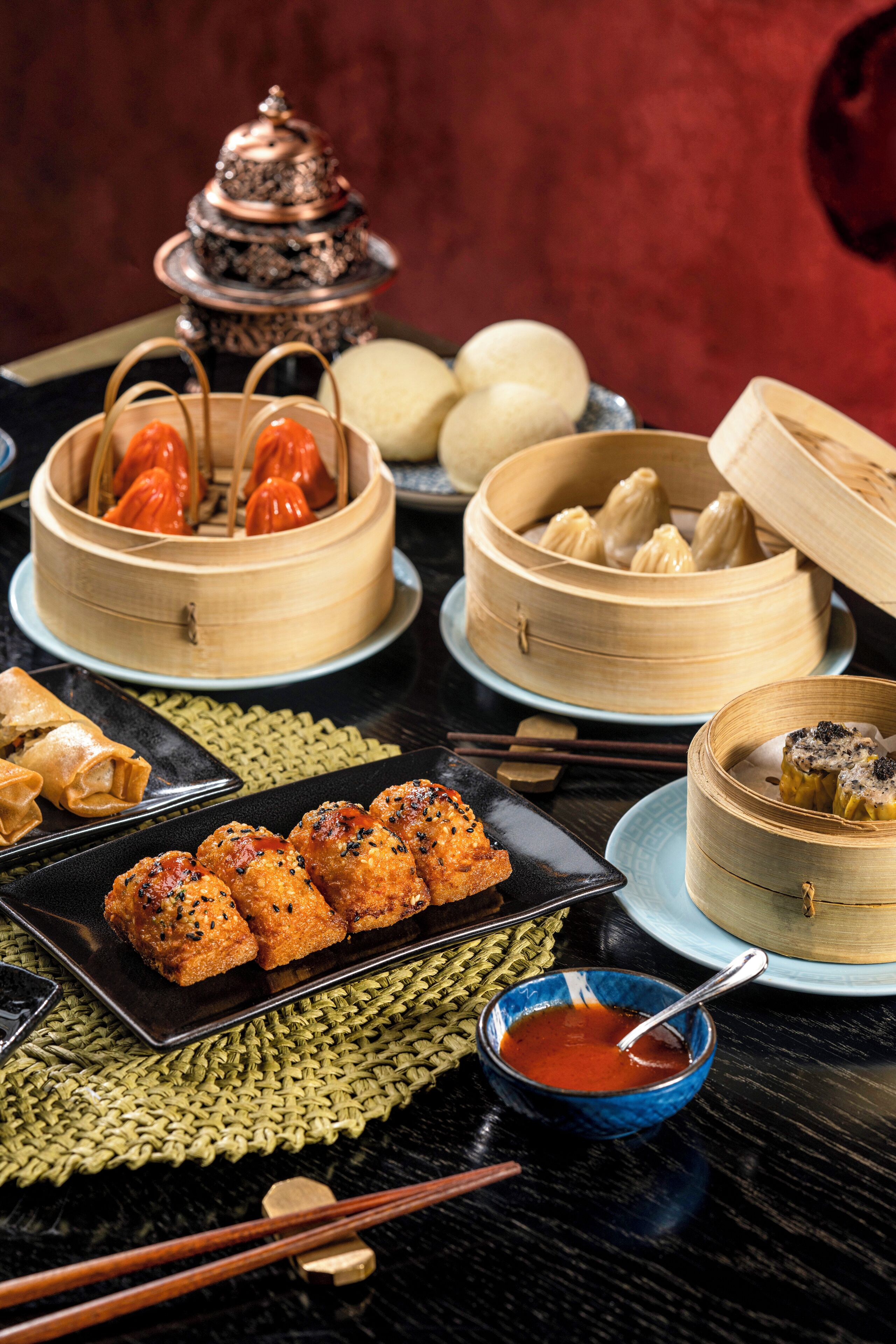 A table with various Chinese dishes, including dumplings and spring rolls, and a traditional copper pot.