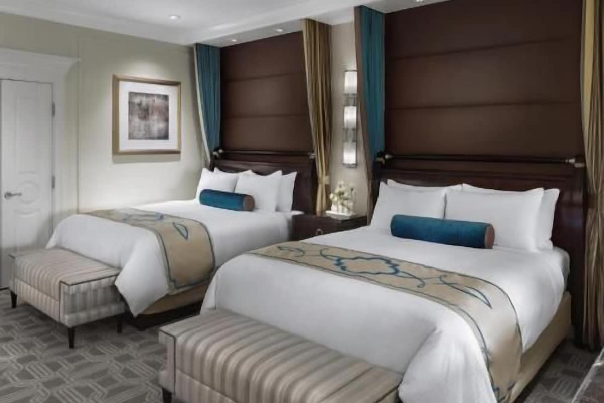 Een hotelkamer met twee bedden, een bankje, een nachtkastje en een lijst aan de muur.