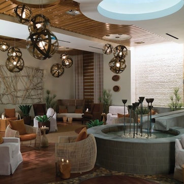 A modern lounge area with wicker furniture, a central water feature, and unique spherical pendant lighting.