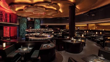 A modern bar area with a circular bar, seating, and a green wall.