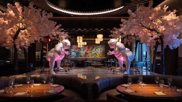 Un restaurante con un escenario central, mesas con copas de vino y dos grandes esculturas iluminadas.
