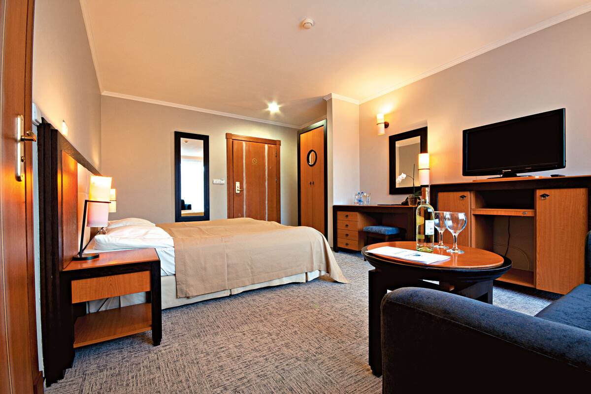 A hotel room with a bed, bedside tables, a desk with a chair, a TV, and a mirror.