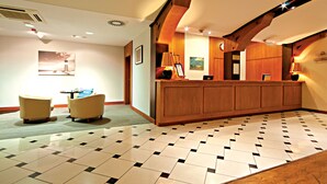 A lobby with a reception desk, two armchairs, and a patterned floor.