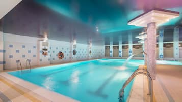 An indoor swimming pool with clear water, tiled walls, and a ceiling with recessed lighting.