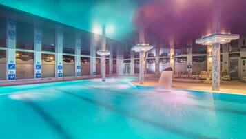 Una piscina interior con agua cristalina, varias pistas de natación y una zona de estar con sillas.