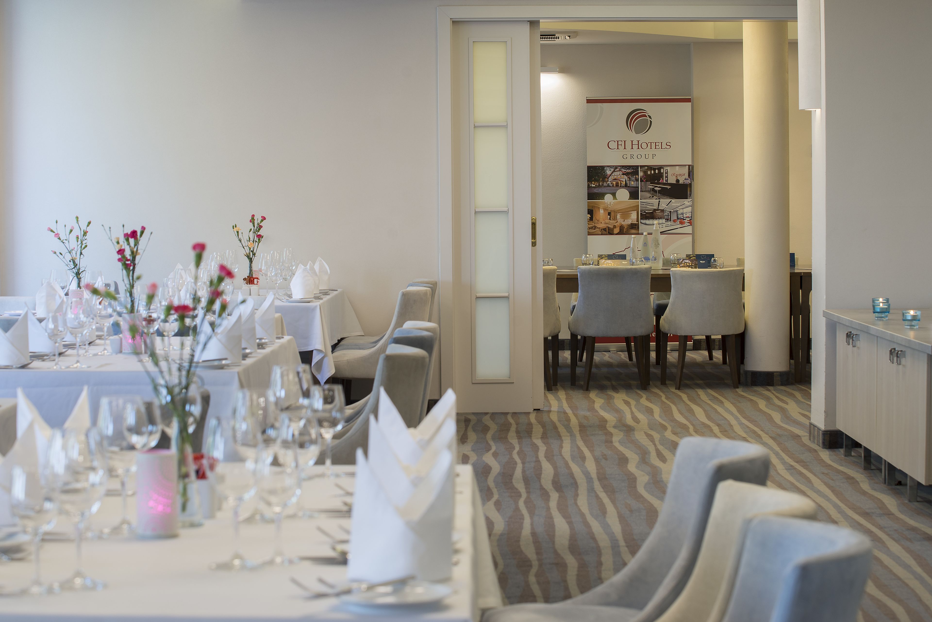 A dining area with tables set for a meal, chairs, and a buffet area in the background.