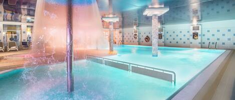 Una piscina interior con una fuente central, paredes de azulejos y zona de baño despejada.