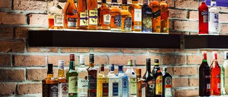 Two shelves of various liquor bottles against a brick wall.