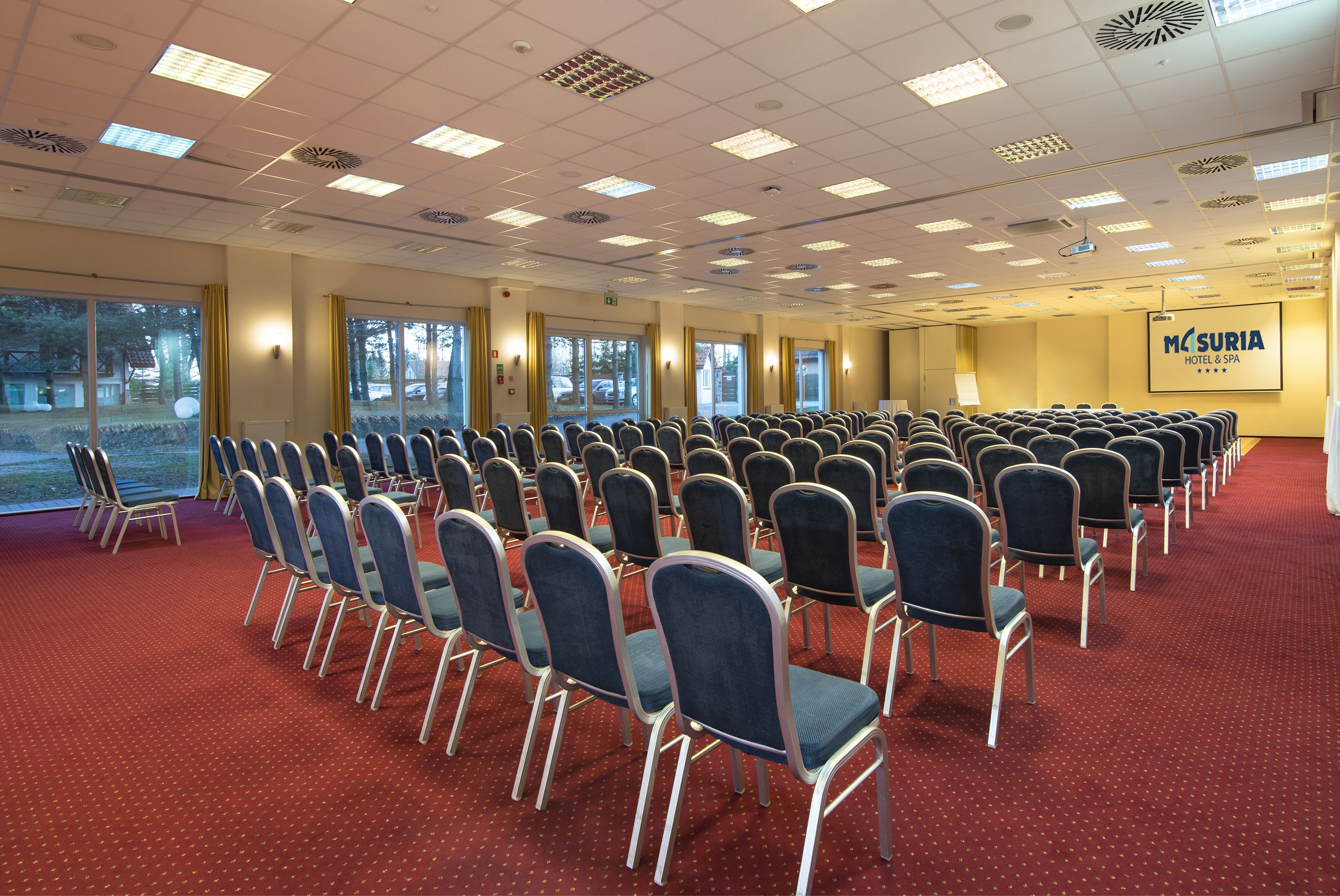 A conference room with rows of chairs, large windows, and a projection screen.