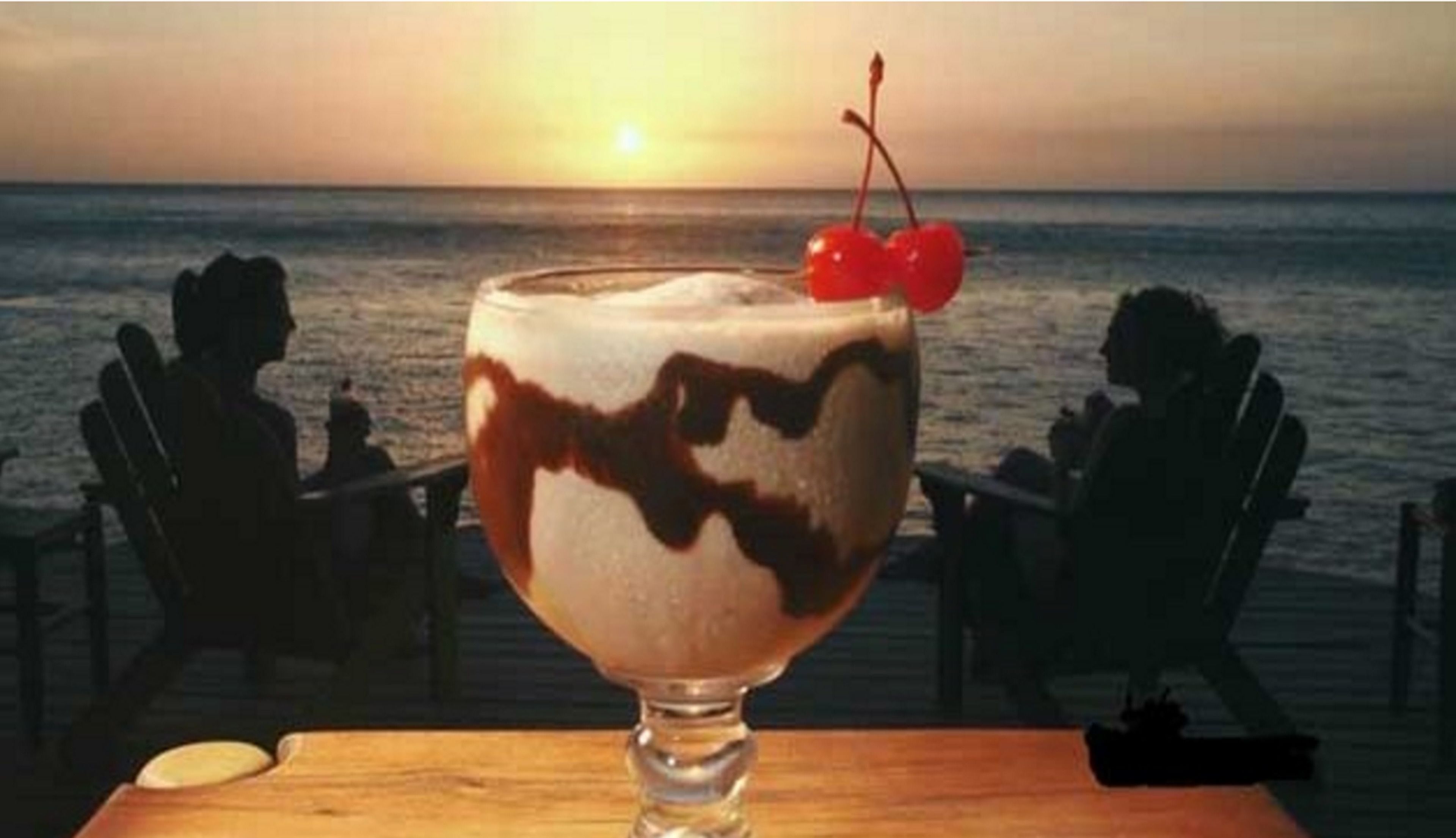 Un vaso de postre con cereza sobre una mesa de madera, con el atardecer de fondo.