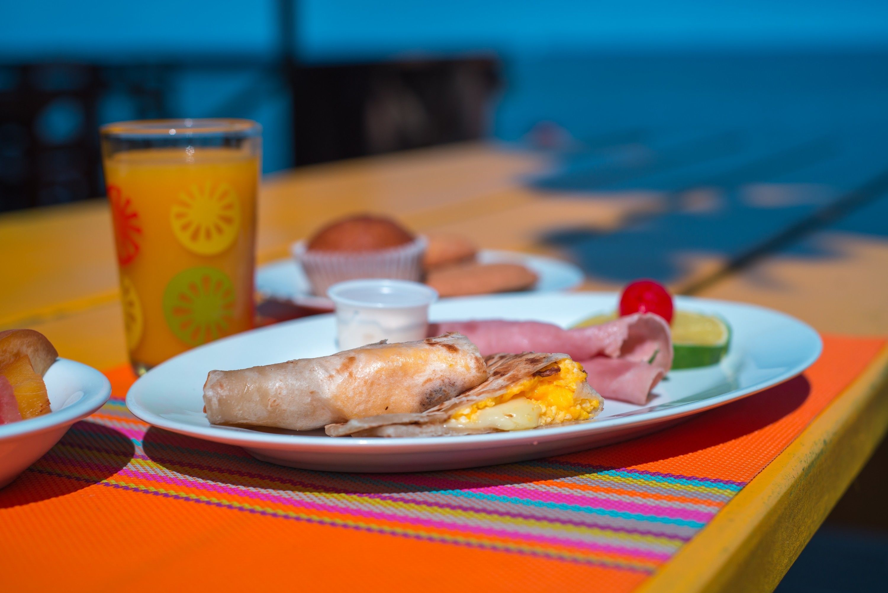 A plate with a wrap, a slice of fruit, and a drink on a colorful tablecloth.