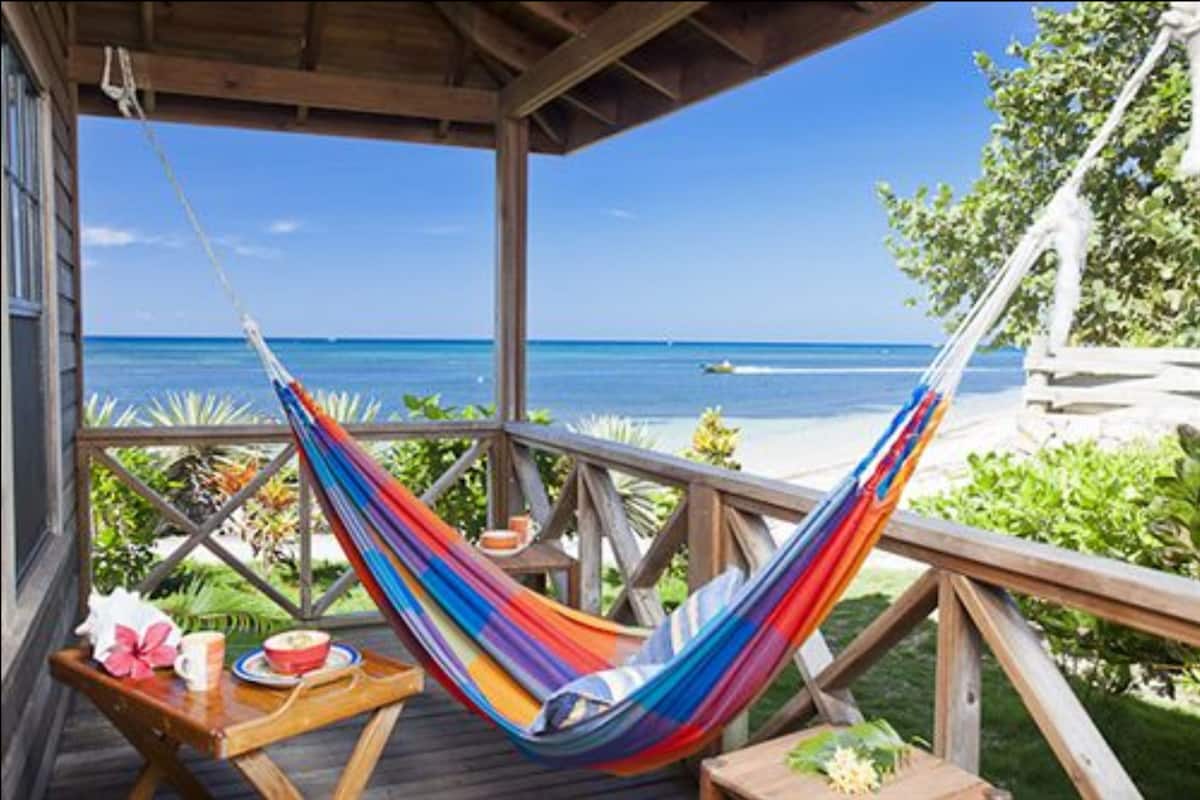A wooden deck with a hammock, a table with a plate and a cup, and a view of the ocean.
