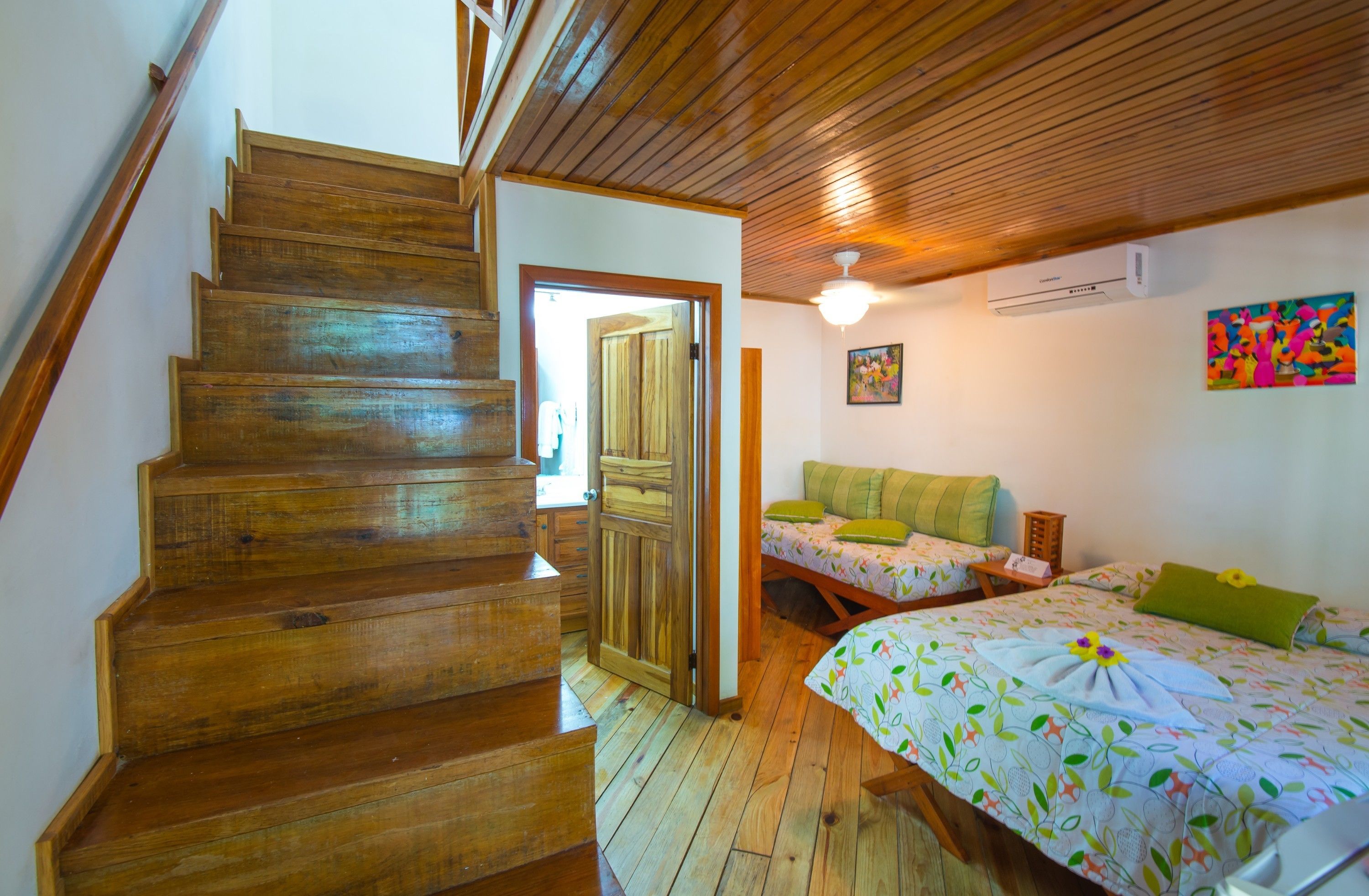 A wooden staircase leading to a bedroom with a bed, a nightstand, and a colorful painting on the wall.