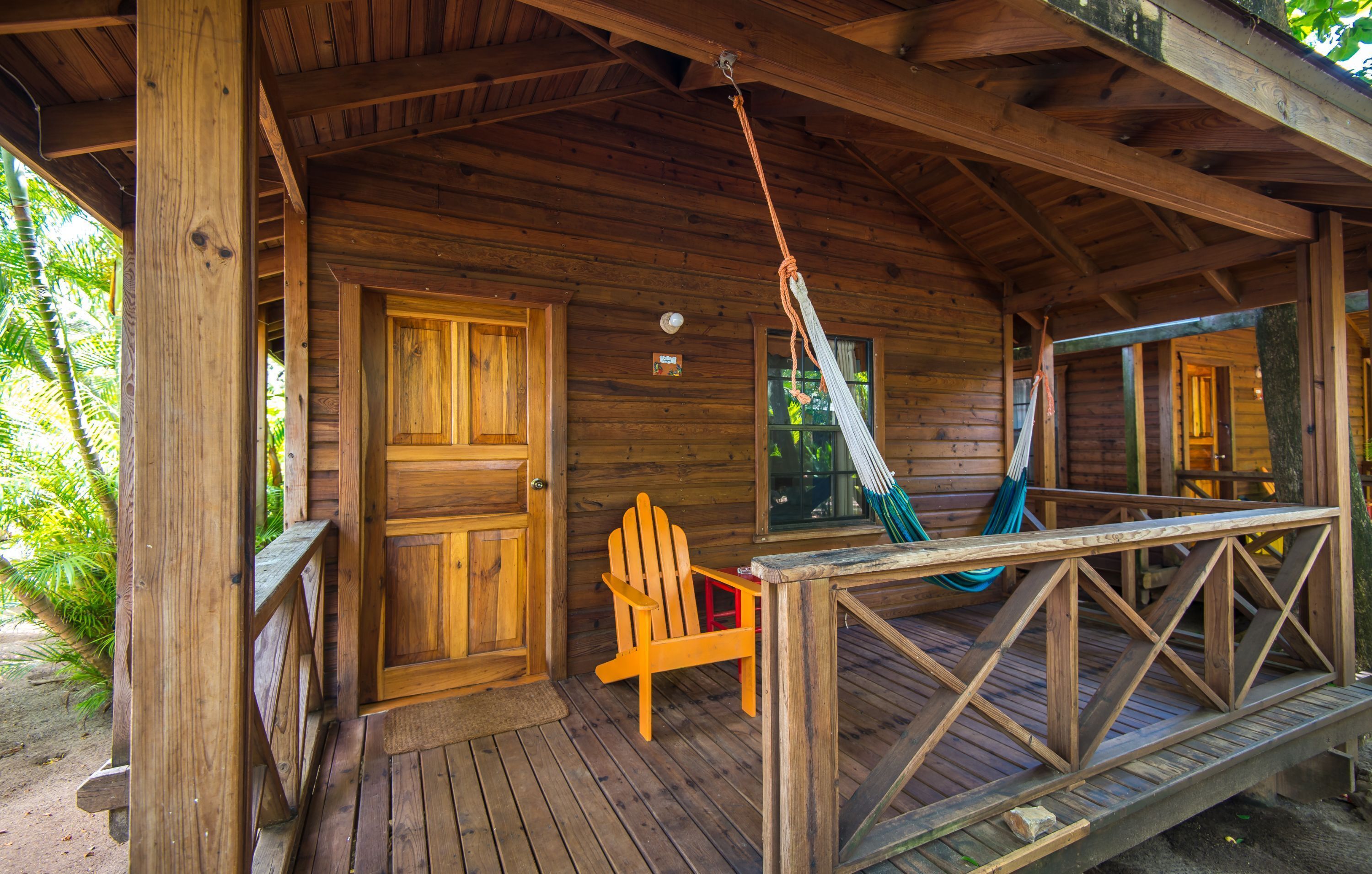 A wooden cabin with a porch, a hammock, and a wooden chair.