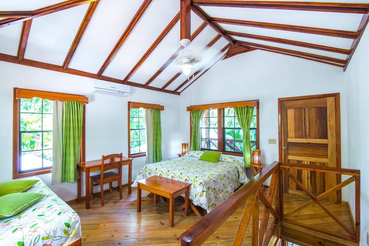A room with a wooden ceiling, a bed with a green pillow, a desk, and a chair.