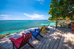 A wooden deck with colorful Adirondack chairs overlooking turquoise waters.
