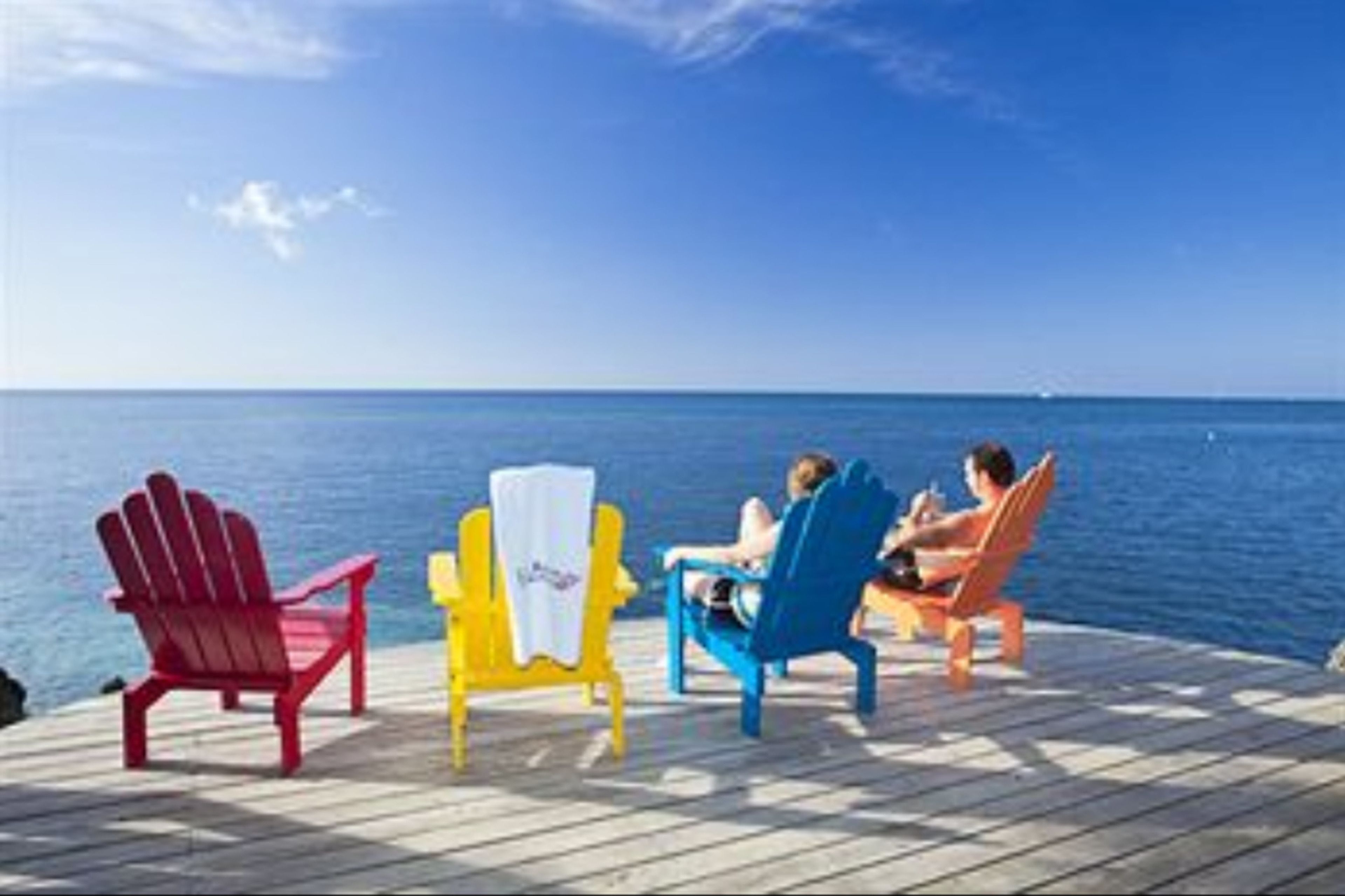 En træterrasse med tre Adirondack-stole, vendt ud mod et roligt hav.