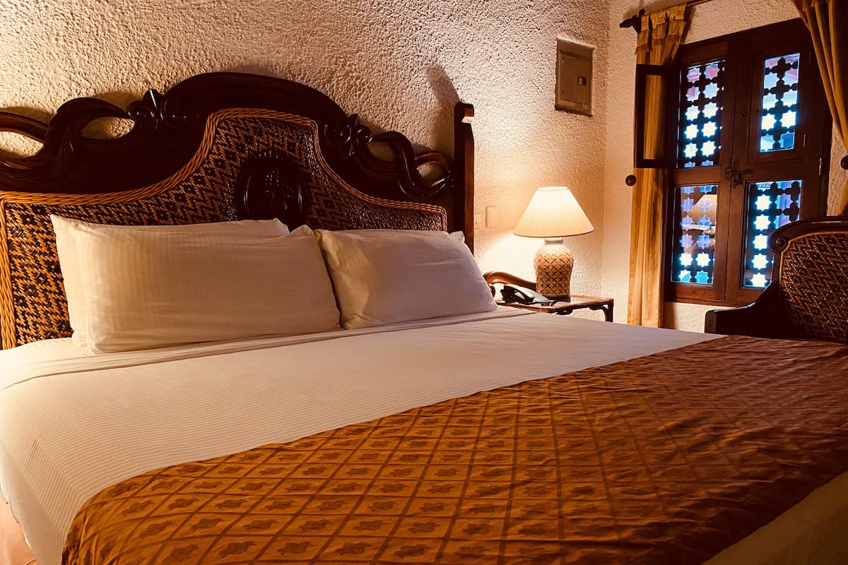 A neatly made bed with a patterned bedspread, a wooden headboard, and a bedside lamp.