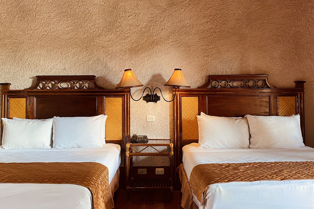 A hotel room with two beds, a wooden headboard, a wall-mounted lamp, and a telephone on a small table.