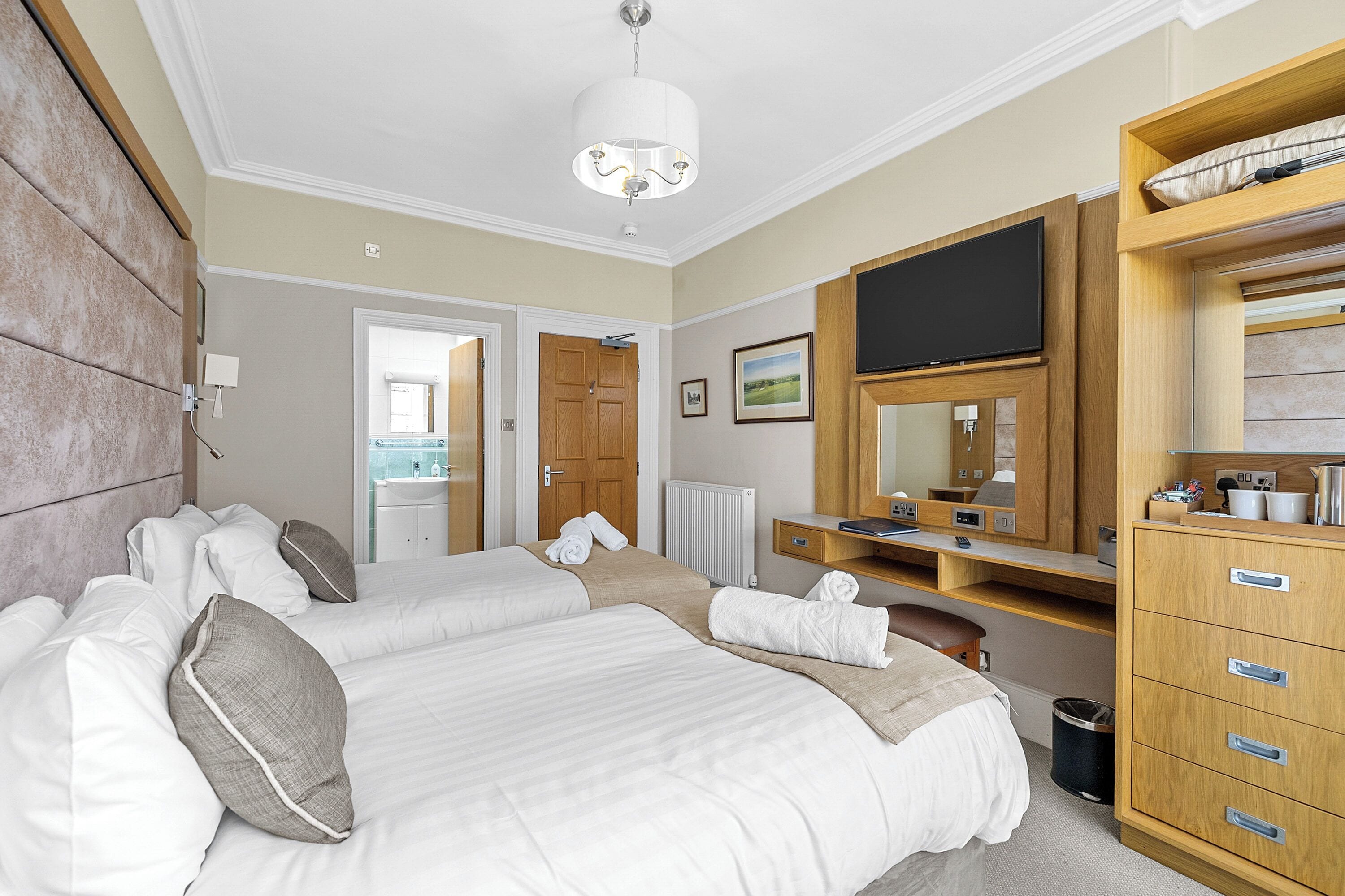 A hotel room with two beds, a TV, a wooden dresser, and a bathroom visible through an open door.