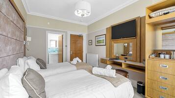 Habitación de hotel con dos camas, un televisor, un aparador de madera y un baño visible a través de una puerta abierta.