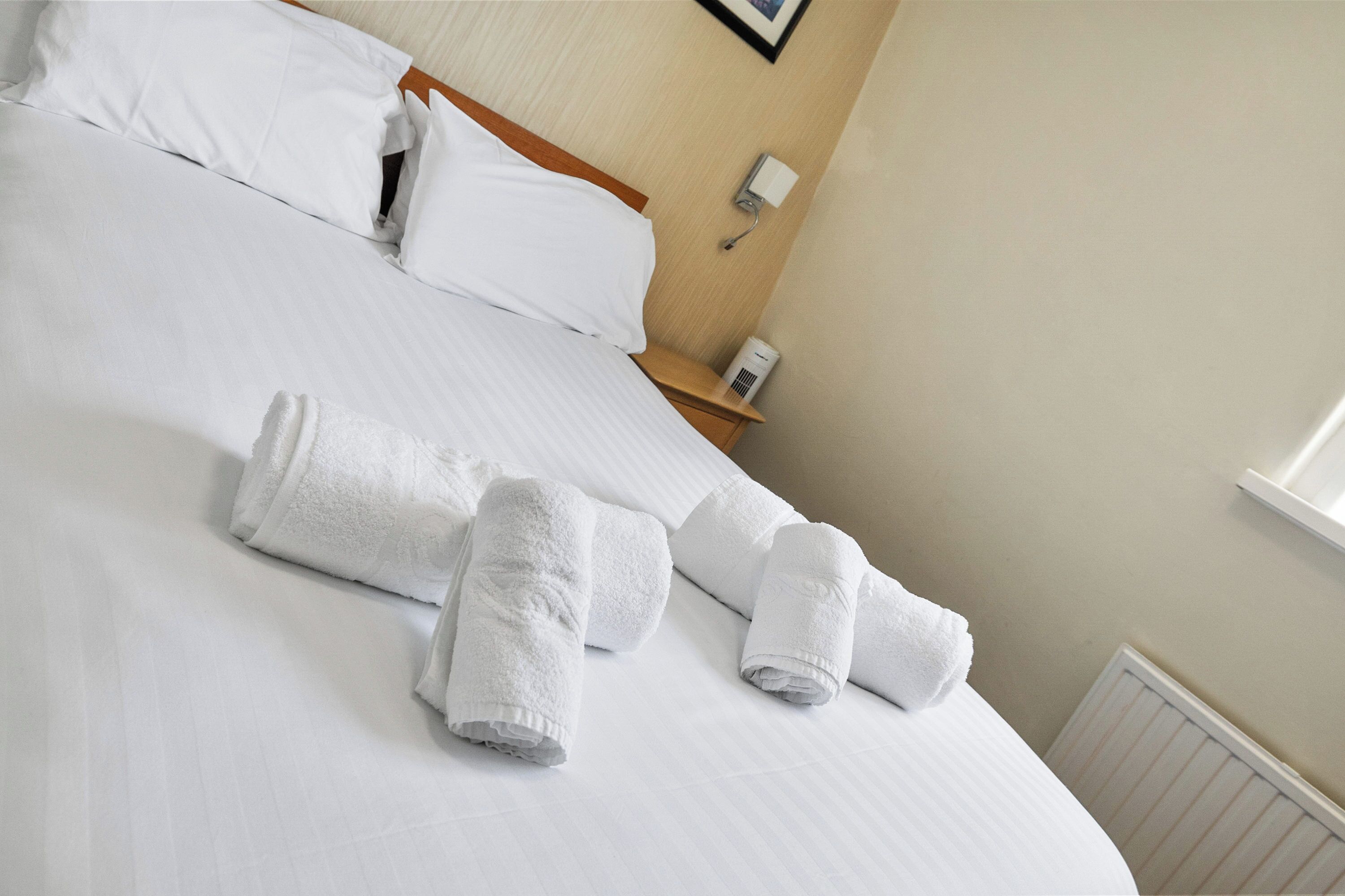 Een net opgemaakt bed met witte lakens en twee opgerolde handdoeken erop.