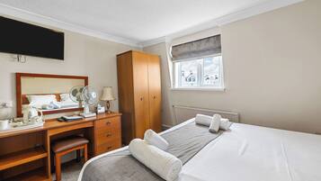 A hotel room with a bed, a desk with a chair, a wardrobe, a window with a view, and a flat-screen TV mounted on the wall.