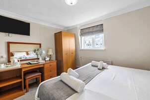 A hotel room with a bed, a desk with a chair, a wardrobe, a window with a view, and a flat-screen TV mounted on the wall.
